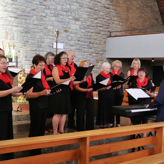 Blick von der Seite auf den singenden Chor. Die Frauen haben schwarze Kleidung an und rote Schals umgebunden.